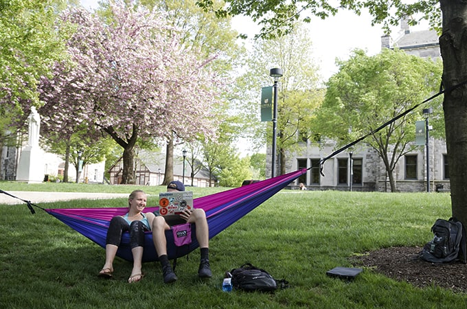 Two students relaxing on a hammock in the shade on the Quad