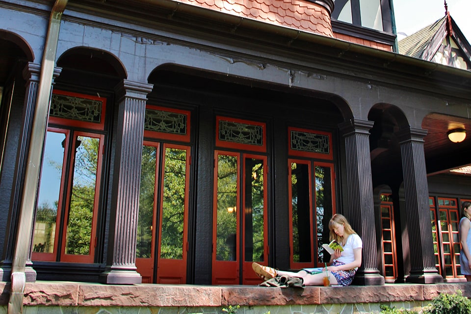 A student sits on the ledge of the porch of the Humanities Building reading a book