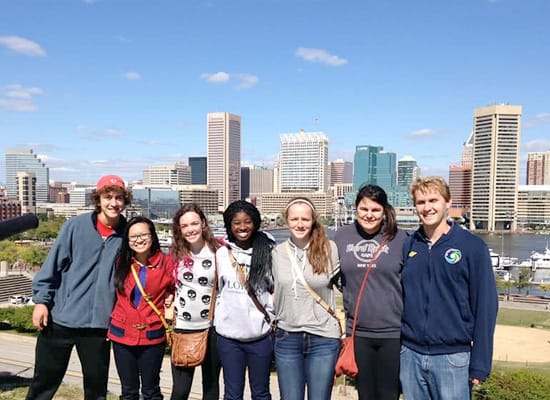 A group of students posing for a photo, with the harbor and Baltimore skyline in the background