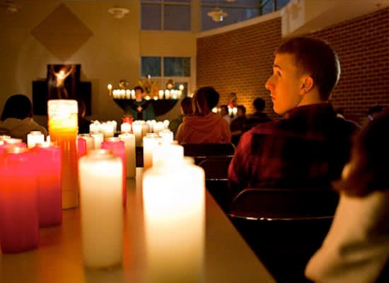 Students sitting during a worship service, with candles lit to the left of them