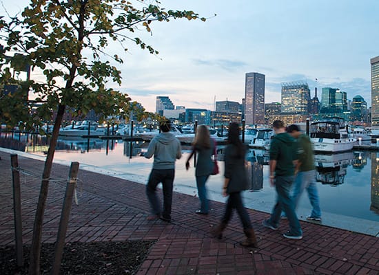 Students walking along the harbor at night with the Baltimore skyline in the background