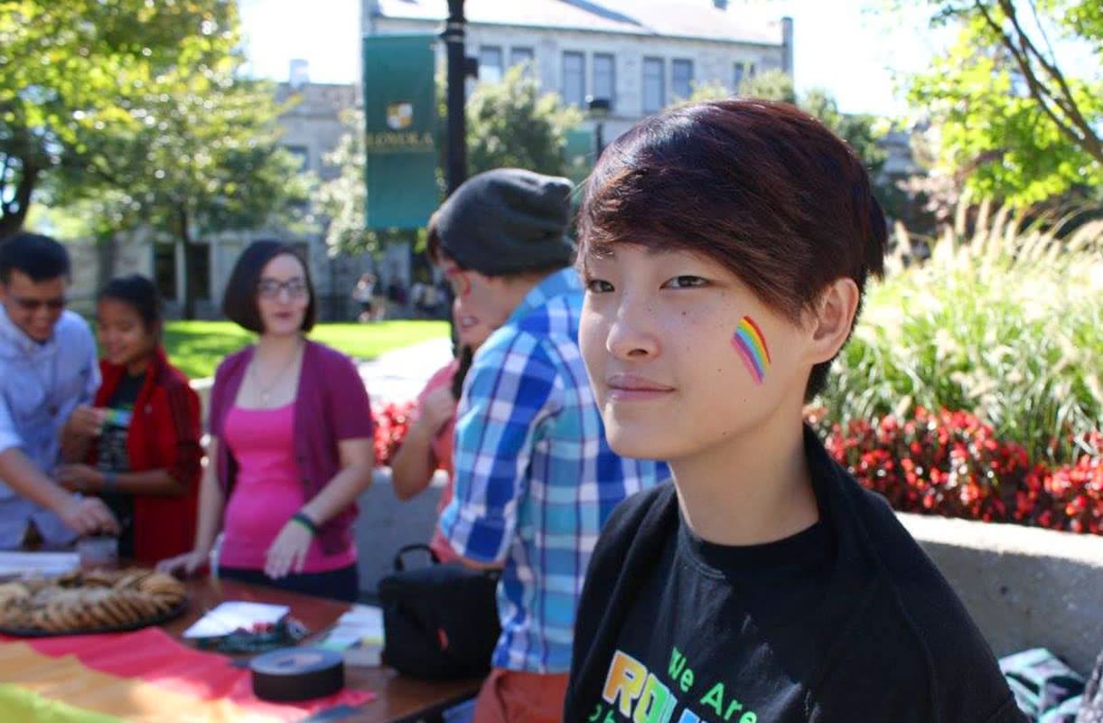 A student with a rainbow painted on her cheek with other students blurred in the background