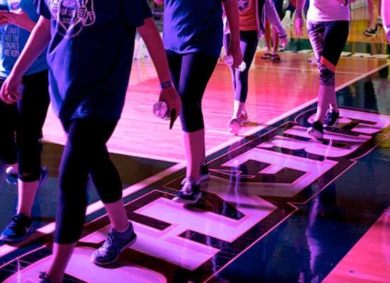 Closeup of students legs walking on a basketball court with purple lighting
