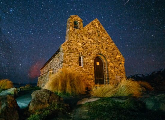 An old, small, stone building sits under the starry, night sky