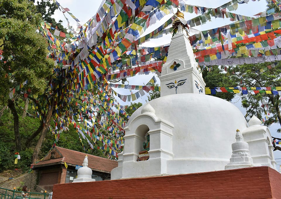 A small, white, stupa with colorful prayer flags hanging above