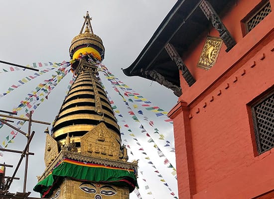 A large stupa with prayer flags next to a red building