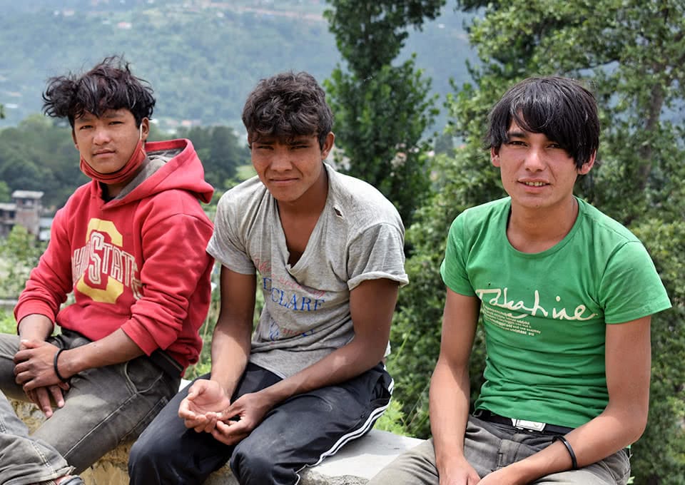 Three teenage boys sit on a short stone wall
