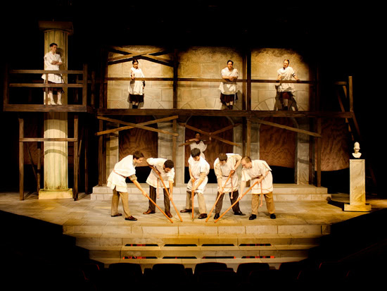 Students holding sticks and wearing white clothes in a roman setting