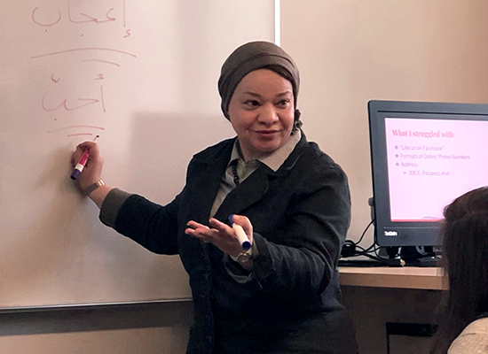 Inas Hassan, Ph.D. in front of a whiteboard, writing and teaching Arabic to her students.