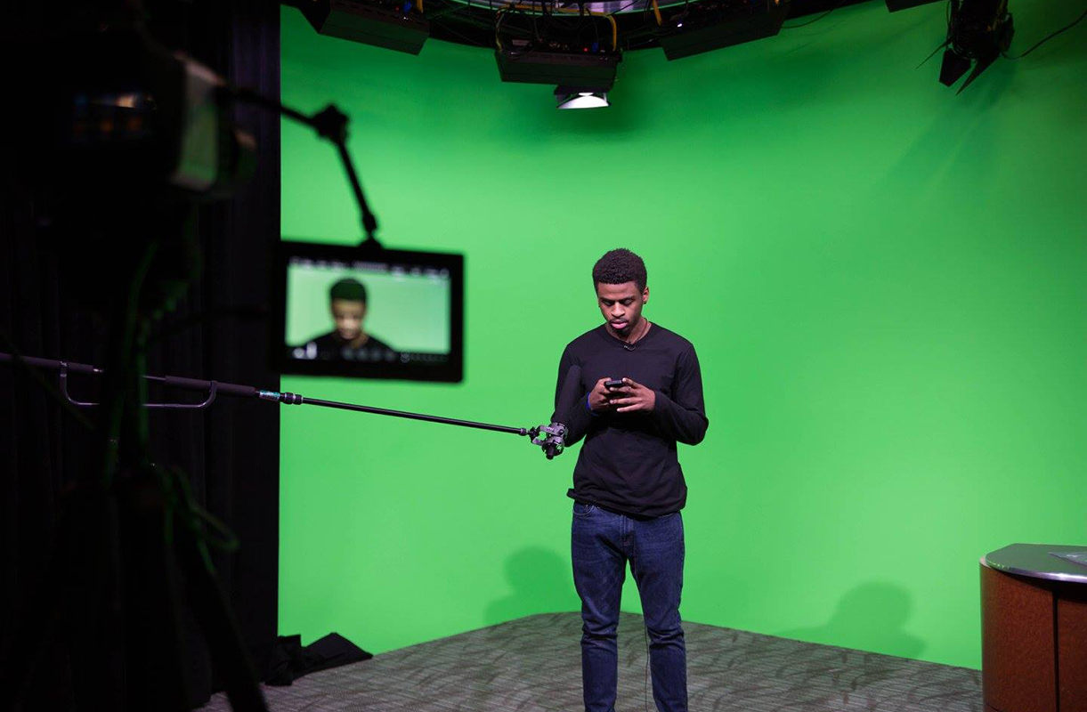 Student stand in front of green screen.