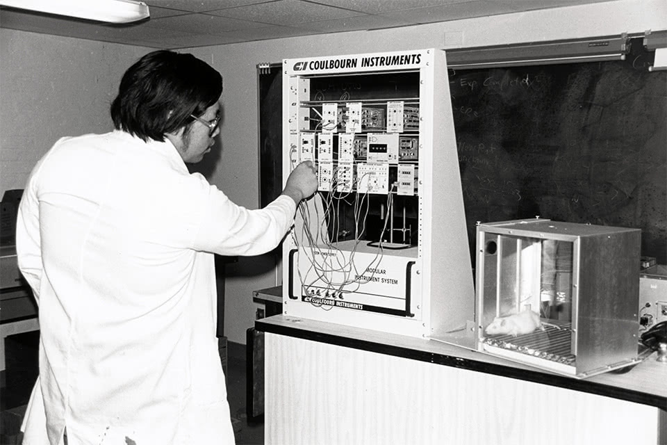 Vintage black and white photo of a student plugging wires into an instrument in a lab