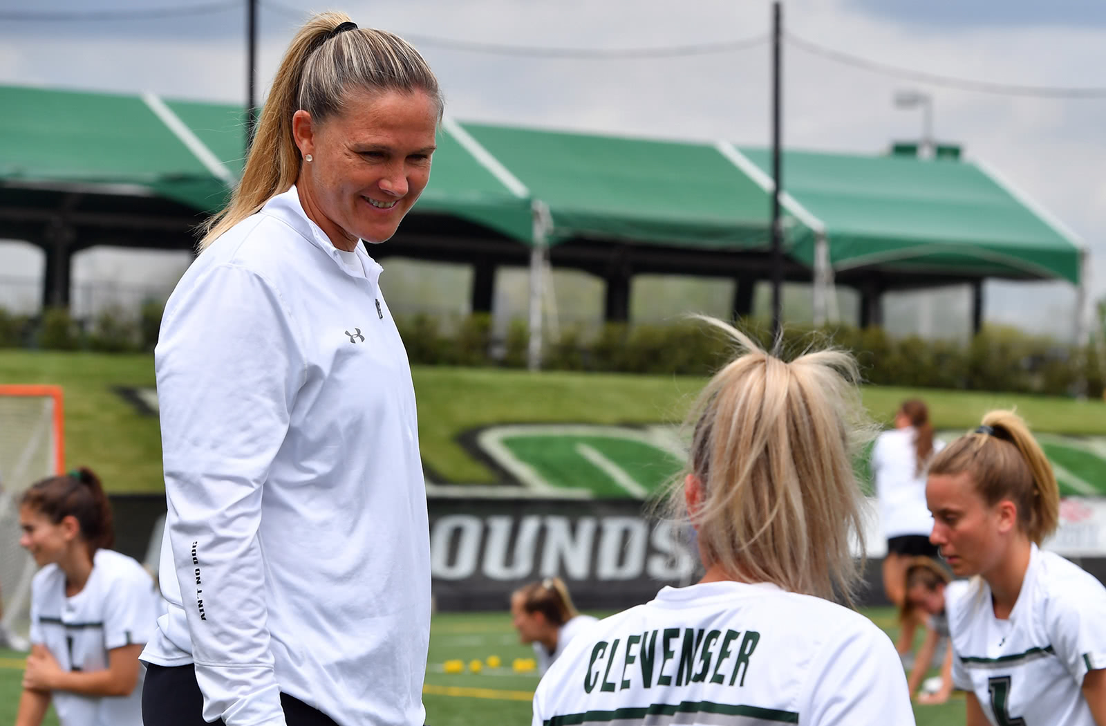 Jen Adams smiling and talking to her lacrosse players during a team practice