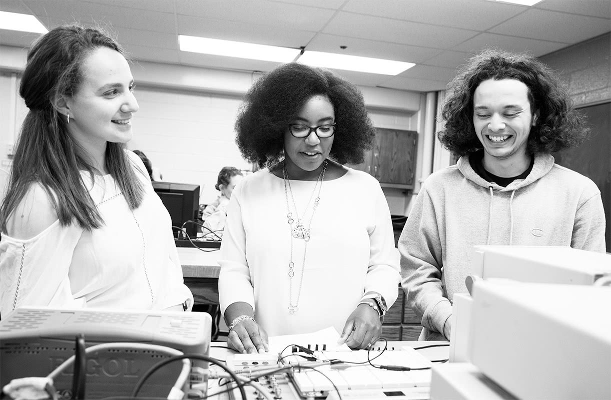 Black and white photo of faculty and students using lab equipment and smiling