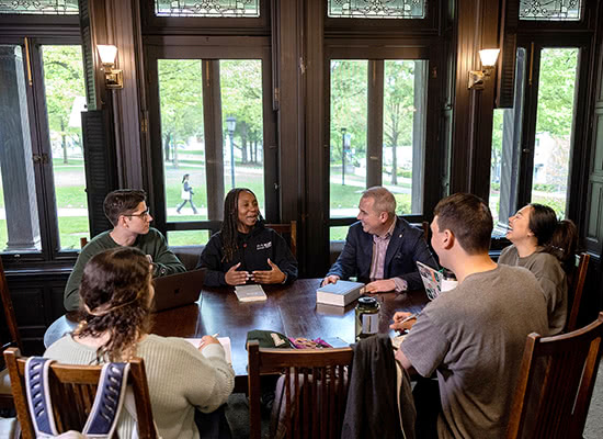President Terry Sawyer and a group of students sitting around a table talking and laughing