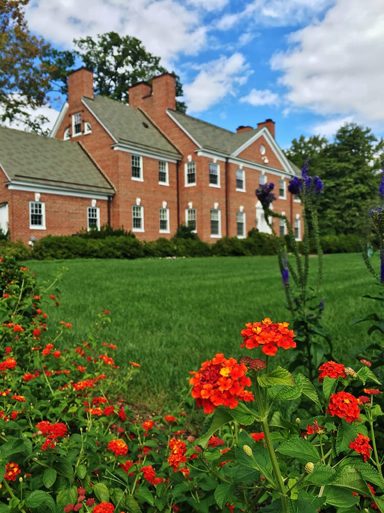 The red-bricked alumni house, with red flowers in the foreground