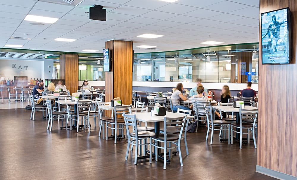 Dining facilities - wood columns, glass windows, faux-wood floor, and students sitting and chatting around tables
