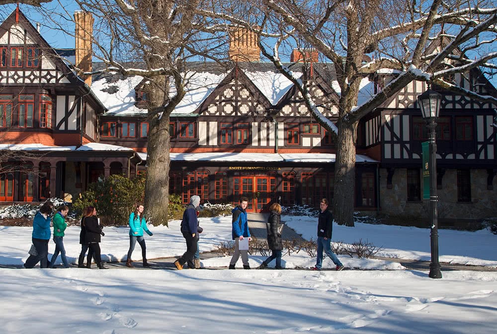 A line of visitors walks in front of the Humanities Building, a fresh blanket of snow covers the ground