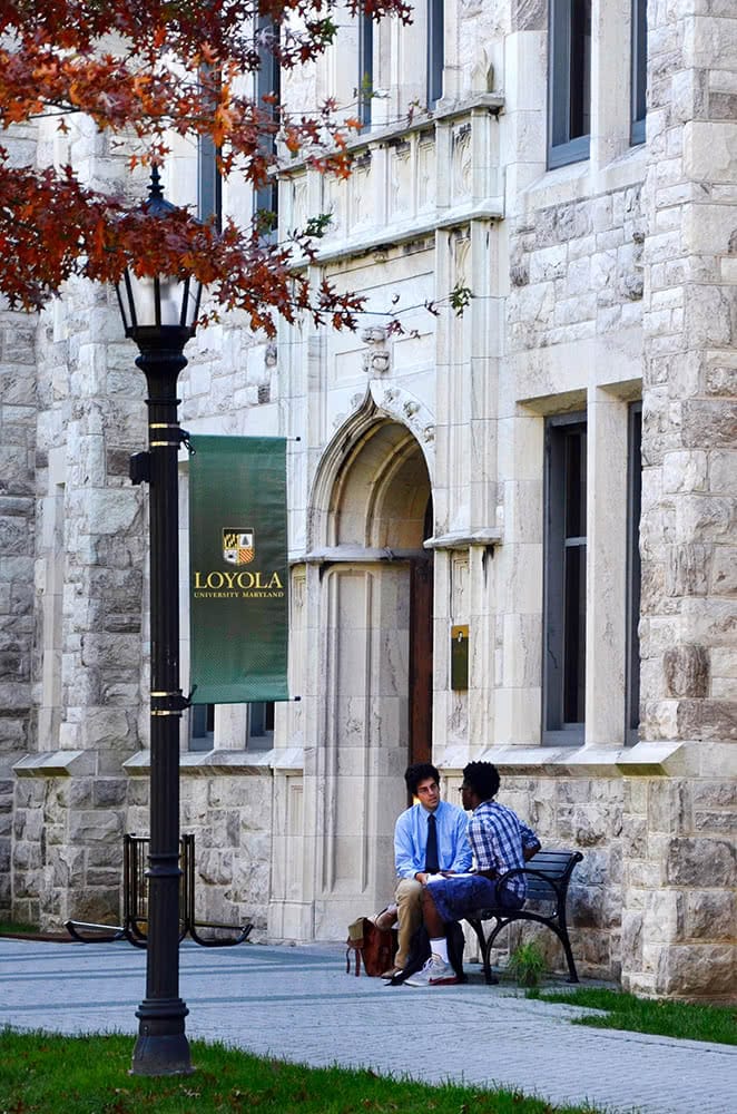 A student and professor sit on a bench in front of Beatty Hall
