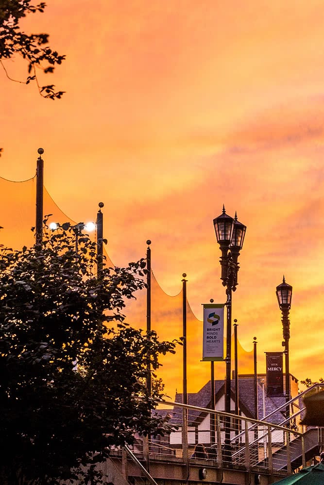 Silhouetted lamp posts and the Humanities Building set in front of an orange sunset
