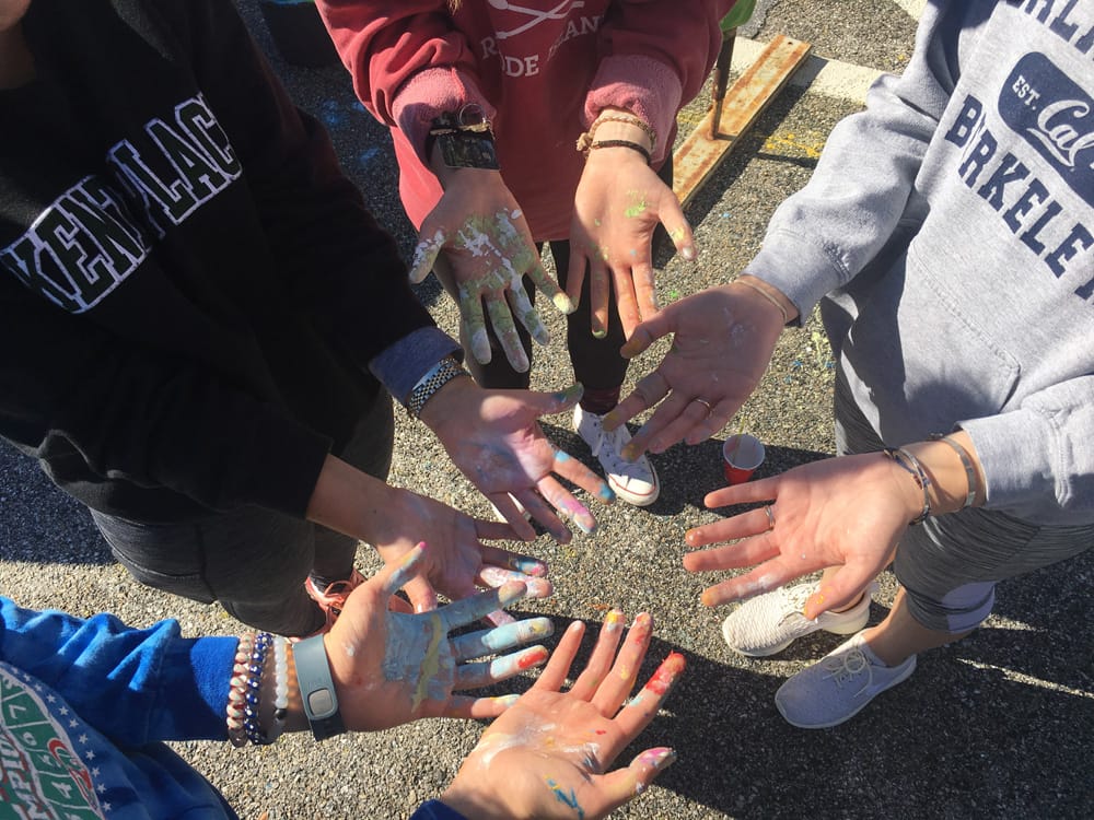 Students standing in a circle with their hands held out, covered in paint