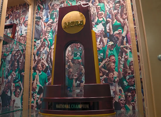 Loyola's NCAA championship trophy in a display case with a photo of fans in the background