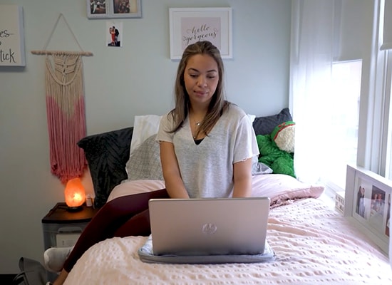 Female student working at laptop on her bed in the residence halls