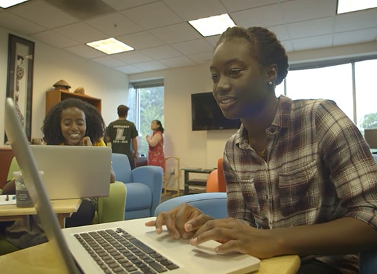 Female students smiling while working at laptops in a student lounge