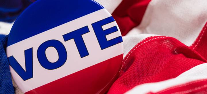 A red, white and blue "vote" Button on an American flag.