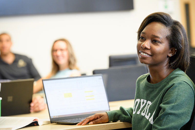 A student sits inside Loyola's Sellinger School of Business and Management with their laptop.