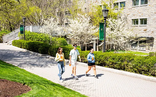 An expansive quad lawn stretches under a partly cloudy sky with students enjoying the weather