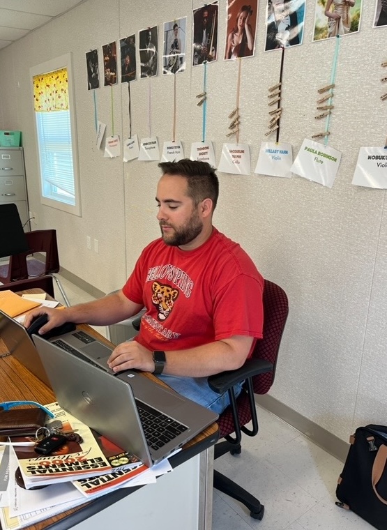 Kevin works on two laptops at his desk in a school setting