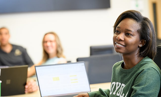 A student smiles at a desk listening to a seminar