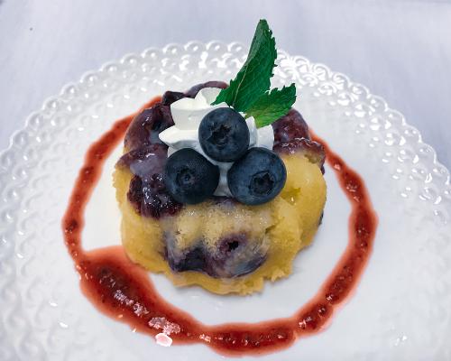 Mini blueberry cake topped with whipped cream and fresh blueberries, artfully arranged on a plate