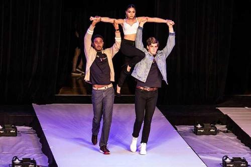 A female model being lifted in the air by her arms by two male models on the runway.