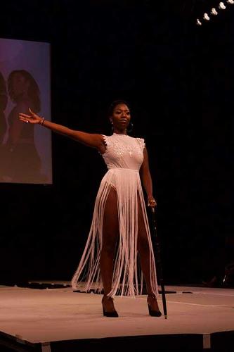 A stunning female model posing with one arm up at the end of the catwalk wearing a high-cut white dress.