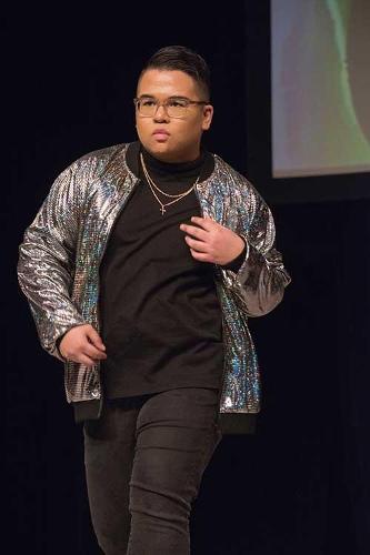 Male model strutting down the catwalk in a vibrant silver jacket and black pants.