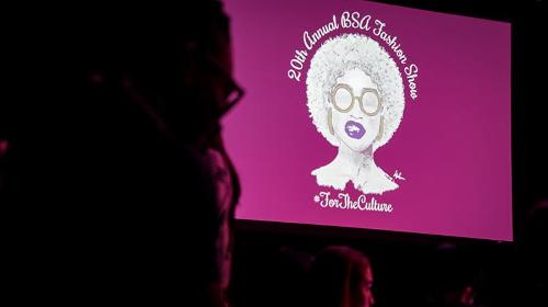 Large screen projection of a woman with glasses, bright lipstick, and an afro with text.