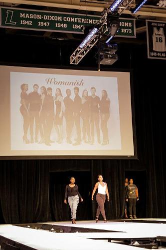 Three models walking under the large projection screen that reads 'womanish' 