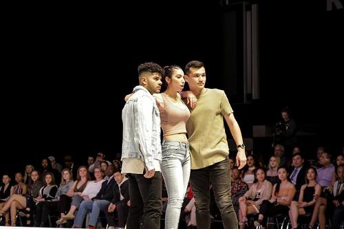 Three models embracing shoulder to shoulder with an audience behind them.