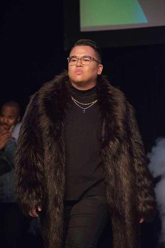 A male model in a big fur coat walking down the catwalk.